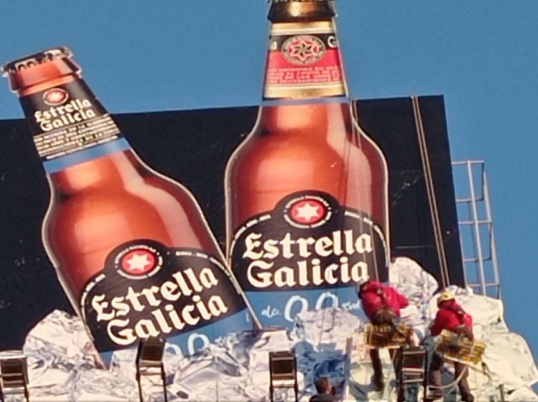 Dos trabajadores colocando una lona vertical grande de cerveza Estrella de Galicia