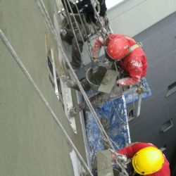 Imagen de tres trabajadores realizando la restauración de una medianera de edificio