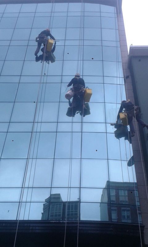 Imagen de tres trabajadores en altura realizando la limpieza de una fachada acristalada