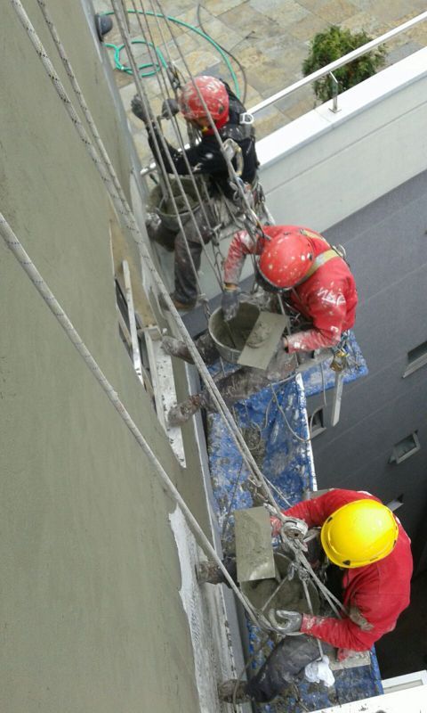 Imagen de tres trabajadores realizando la restauración de una medianera de edificio