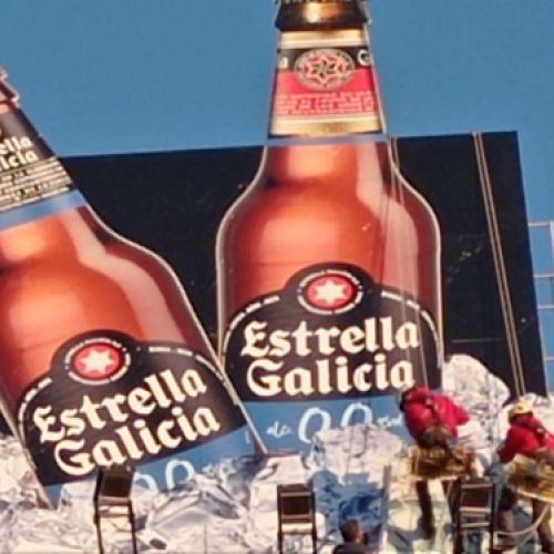 Dos trabajadores colocando una lona vertical grande de cerveza Estrella de Galicia