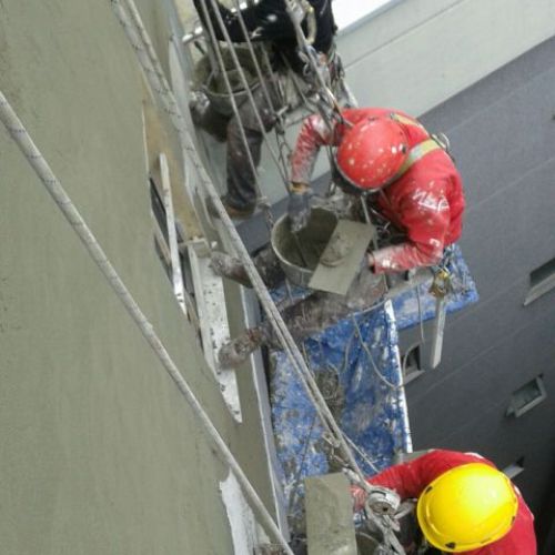 Imagen de tres trabajadores realizando la restauración de una medianera de edificio