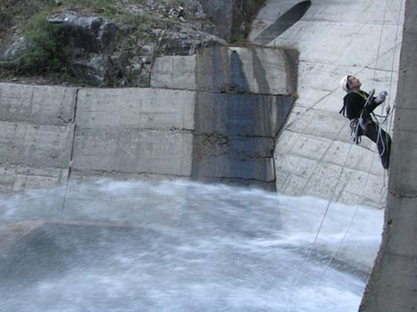 Imagen de trabajador colgado el altura con arneses en pared de presa