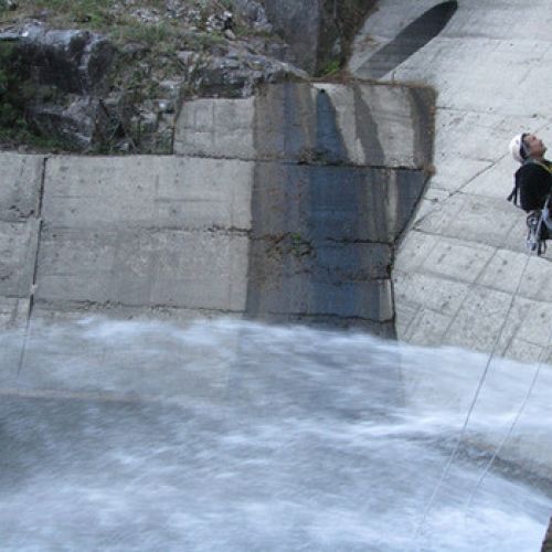 Imagen de trabajador colgado el altura con arneses en pared de presa