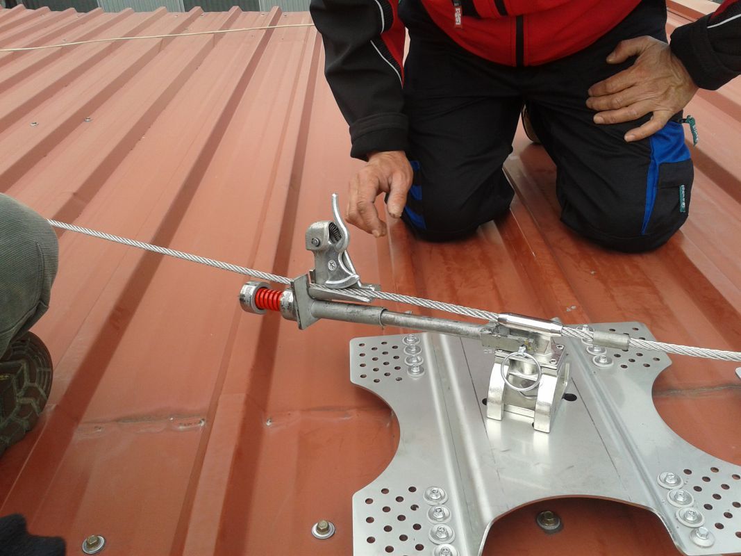 Imagen de trabajador tensando el cable de una línea de vida colocada en tejado