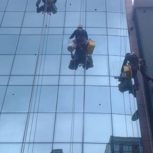 Imagen de tres trabajadores en altura realizando la limpieza de una fachada acristalada