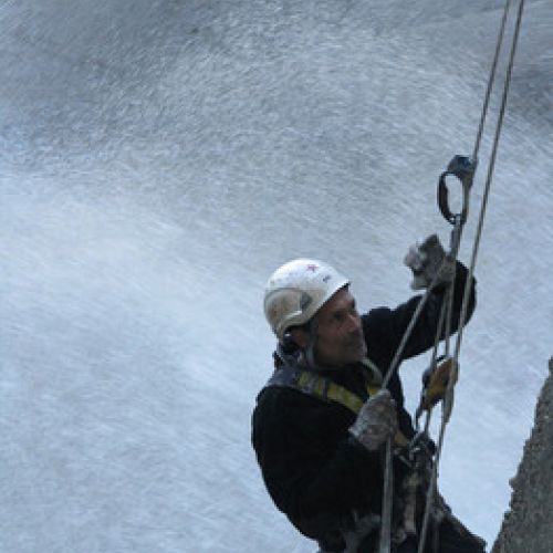 Primer plano de trabajador colgado el altura con arneses en pared de presa